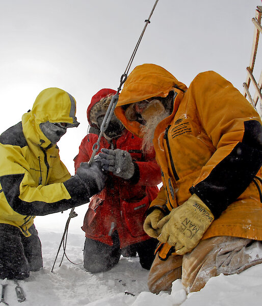 Three expeditioners outdoors gathered around a cable