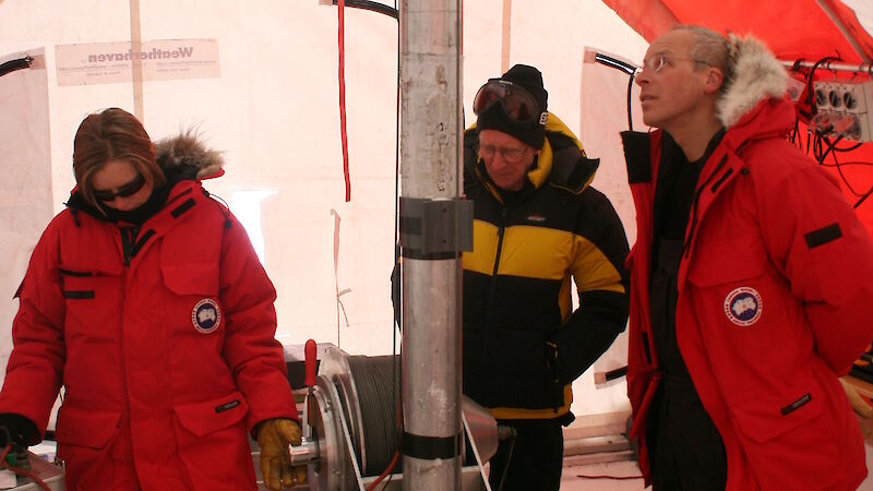 Three Antarctic scientists watch the ice core drill inside a drilling tent at Law Dome.