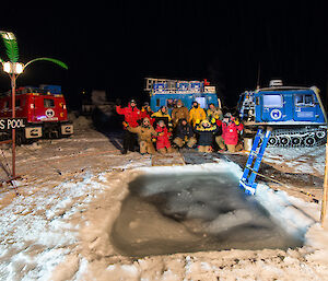 A group photo of Davis station expeditioners in front of the hole cut in the sea ice for the midwinter swim.