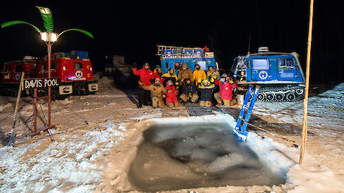 A group photo of Davis station expeditioners in front of the hole cut in the sea ice for the midwinter swim.