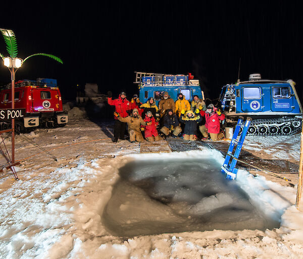 A group photo of Davis station expeditioners in front of the hole cut in the sea ice for the midwinter swim.