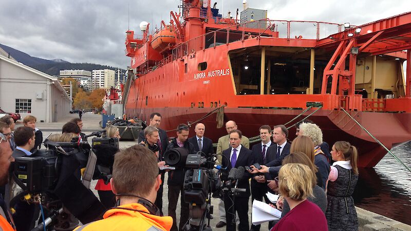 Environment Minister Greg Hunt surrounded by media in front of the orange icebreaker ship Aurora Australis on Hobart's waterfront.