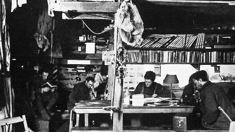 A winter afternoon in the living hut at Commonwealth Bay. (L-R) Dr Xavier Mertz (reading), Archie McLean, Cecil Madigan, and John Hunter.