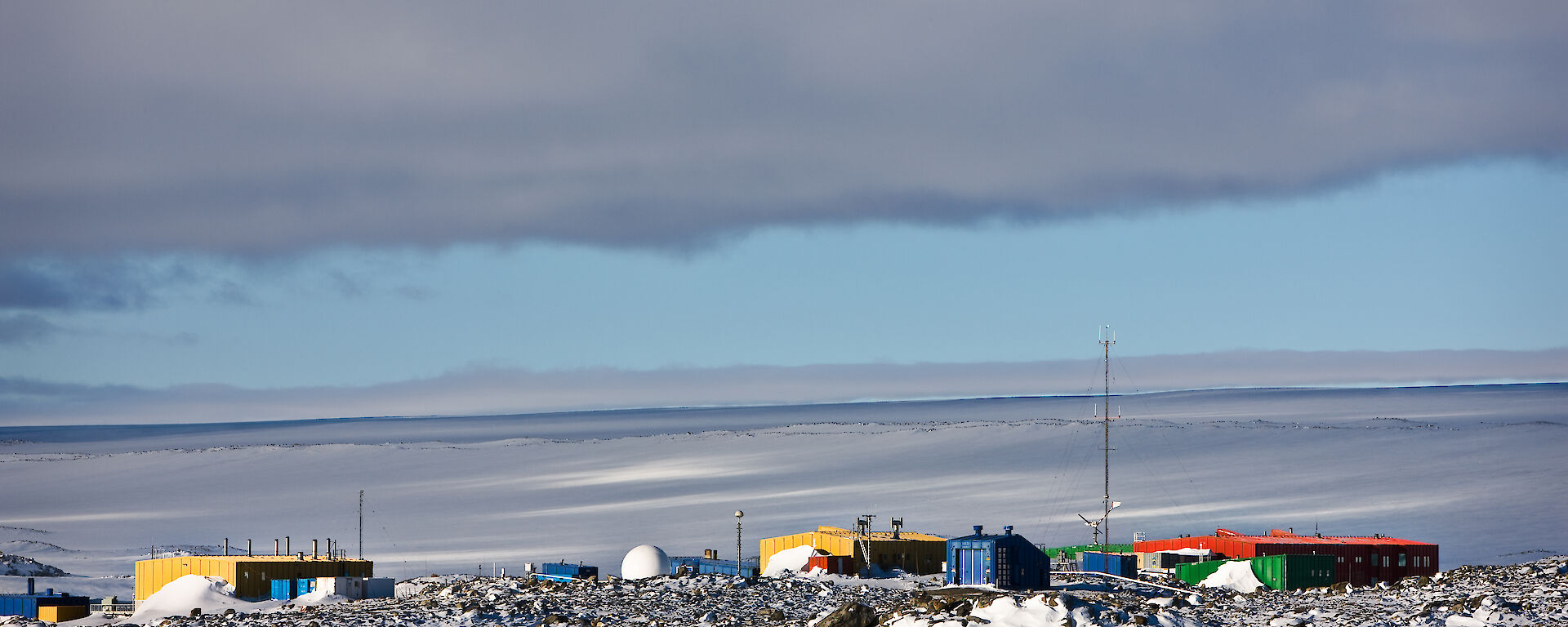 The buildings of Casey station are coloured in reds, yellows and greens and surrounded by ice.