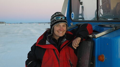 Female expeditioner stands by a blue vehicle.