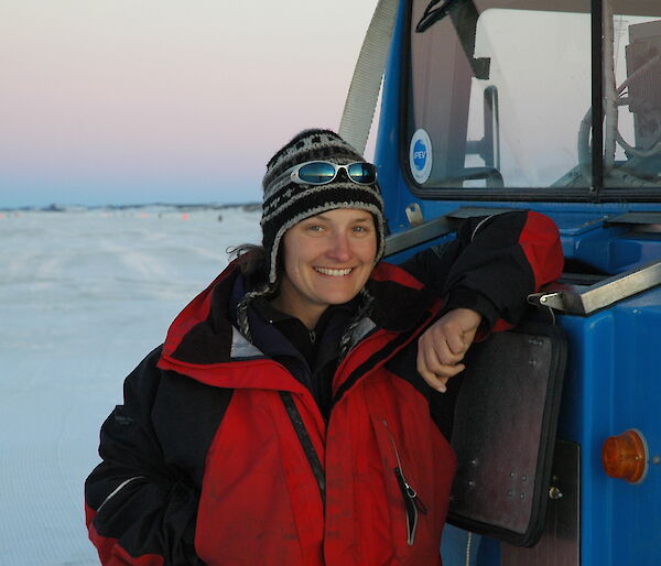 Female expeditioner stands by a blue vehicle.