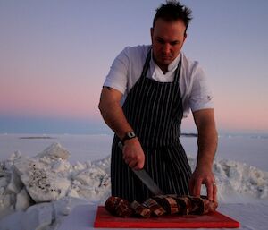 A chef cuts up meat while working outside on the ice.