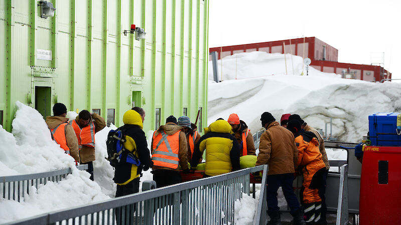 Line of expeditioners pass a stretcher from the building into the back of a Hagglunds vehicle.