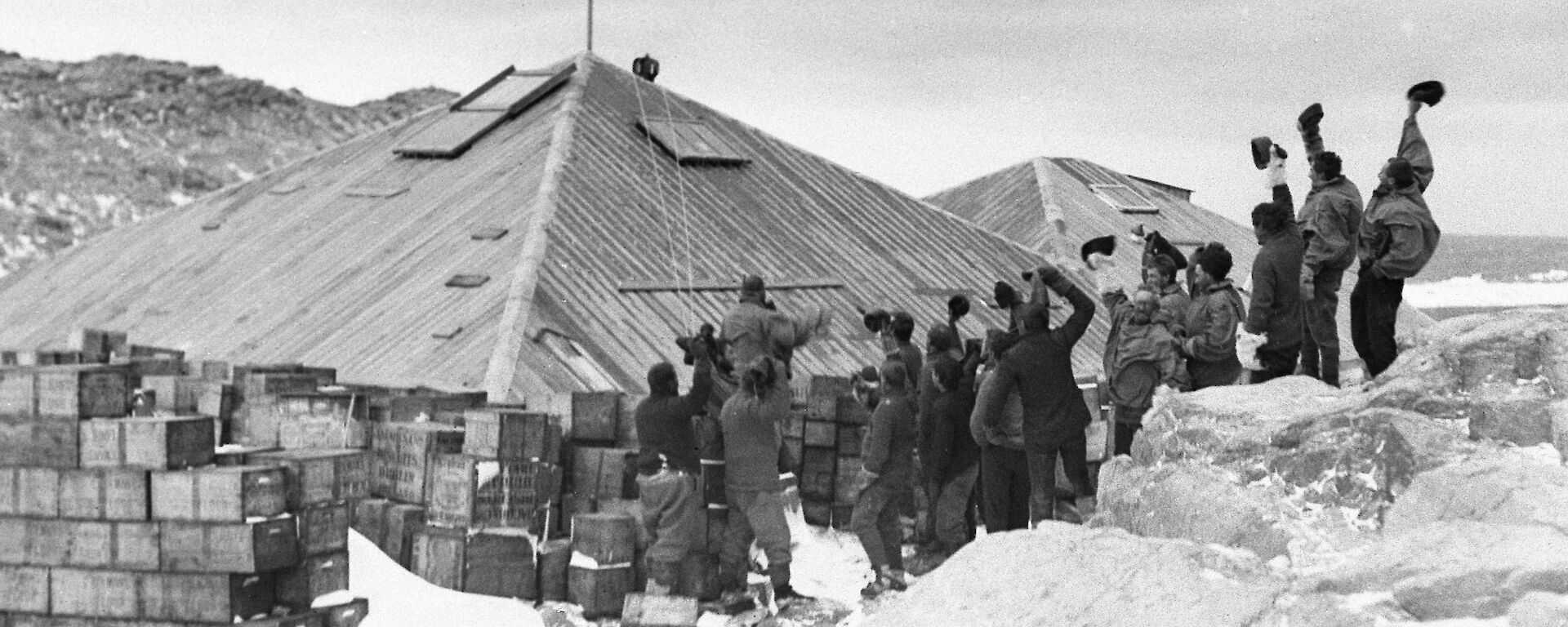 AAE expeditioners raising the flag on the completed huts at Commonwealth Bay