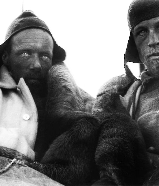 Two men wearing woollen beanies and hunching to keep warm stare at the camera with weathered faces.