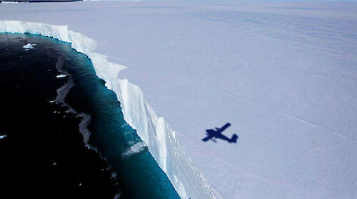 Twin Otter flying across ice cliffs near Casey station