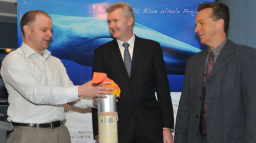 Mike holds the tall silver canister that houses the sonobuoy with a red float at the top.