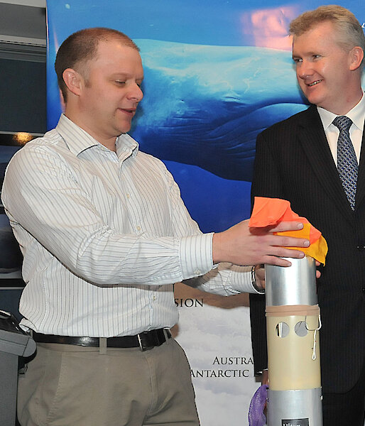 Mike holds the tall silver canister that houses the sonobuoy with a red float at the top.