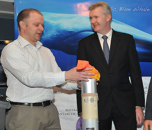 Mike holds the tall silver canister that houses the sonobuoy with a red float at the top.