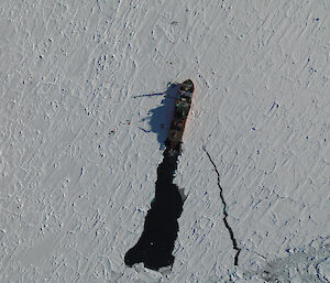 An aerial photograph taken with the high resolution digital camera in the helicopter, showing part of a survey area or ‘transect’ to the left of the ship with scientists working on the ice. The roughness of the snow cover is discernible. (Photo: Jan Lieser)