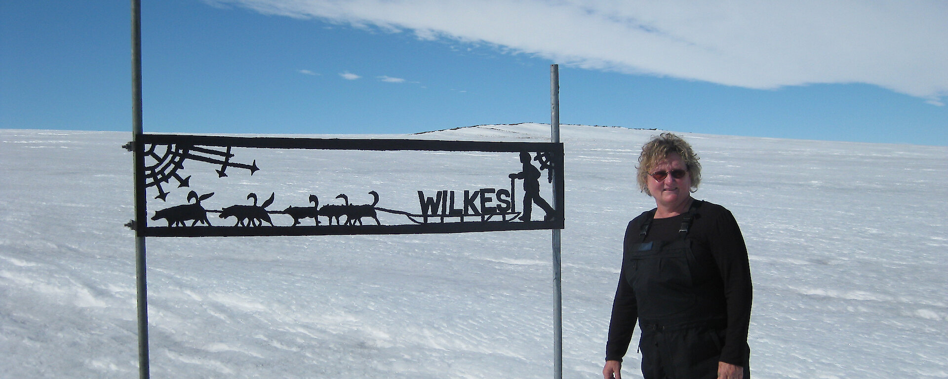 Lyn Maddock beside sign for Wilkes station