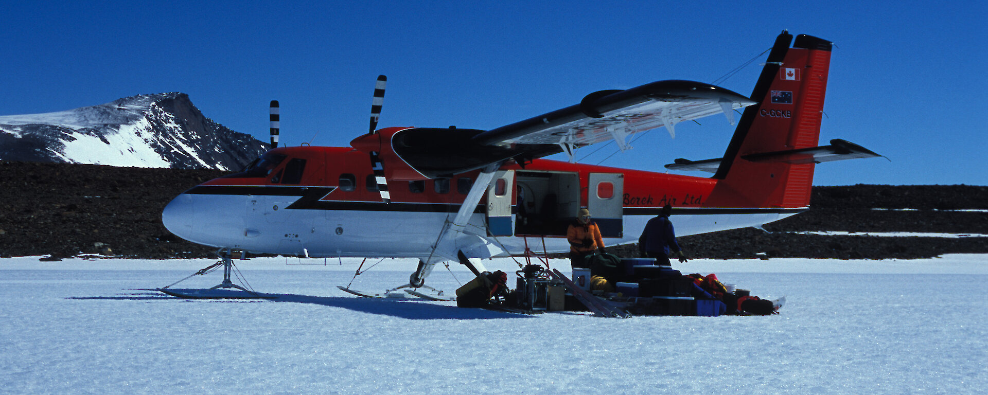 Plane parked on ice with people unloading gear from rear door