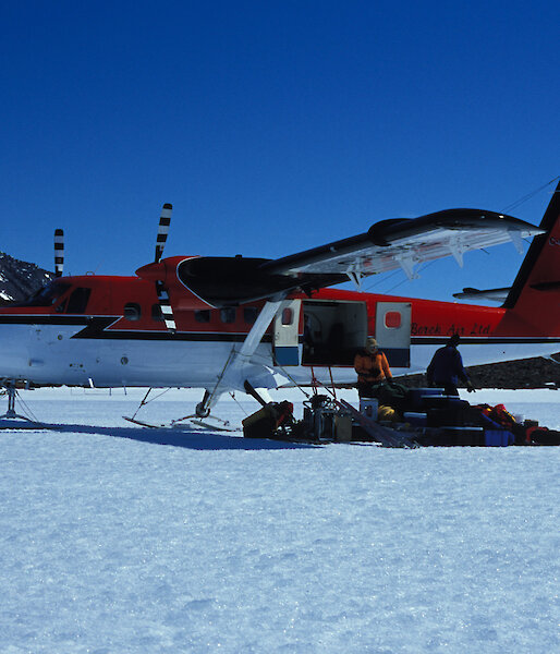 Plane parked on ice with people unloading gear from rear door