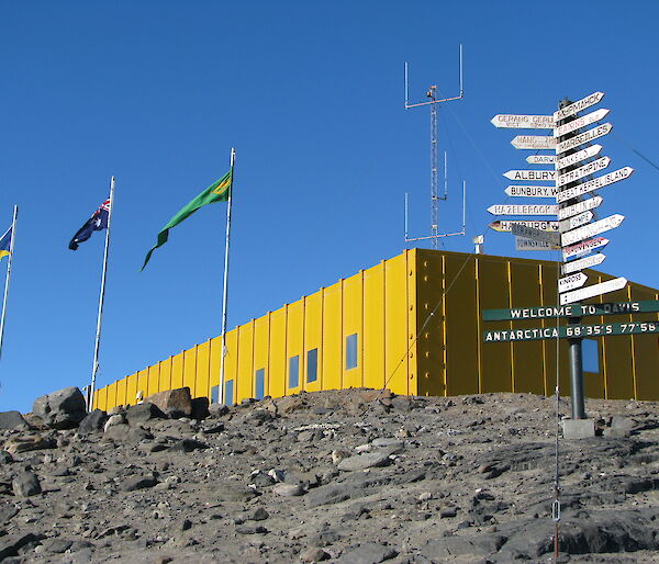 Square yellow building with three flagpoles and a multi-directional sign
