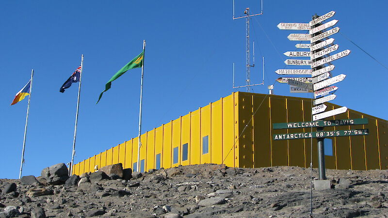Square yellow building with three flagpoles and a multi-directional sign