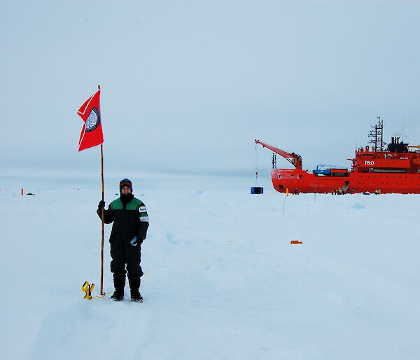 Alex standing on the sea ice and the Aurora Australis behind, during the Sea Ice Physics and Ecosystem eXperiment voyage in 2007.