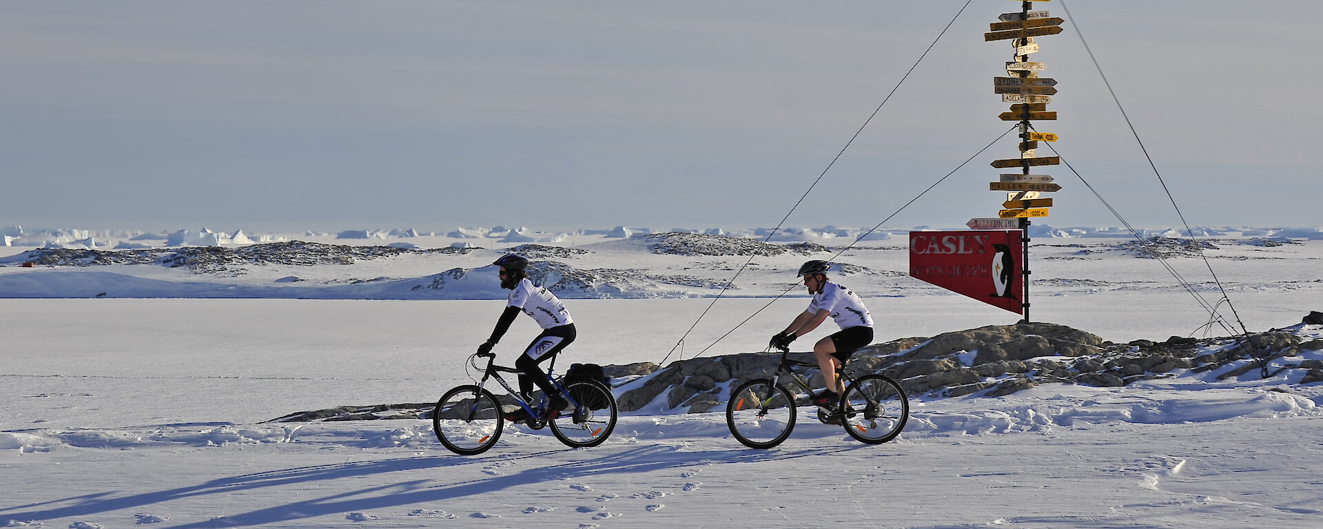 Two expeditioners cycling past sign post