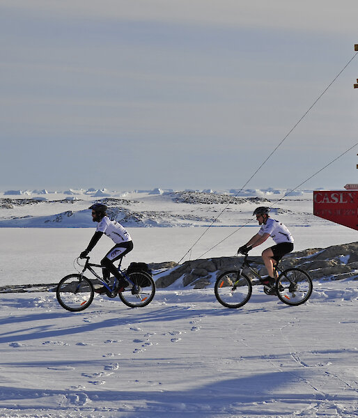 Two expeditioners cycling past sign post