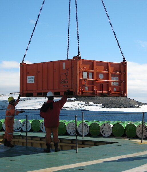 Workers on the Aurora Australis use a crane to unload cargo as part of resupply operations at Davis station