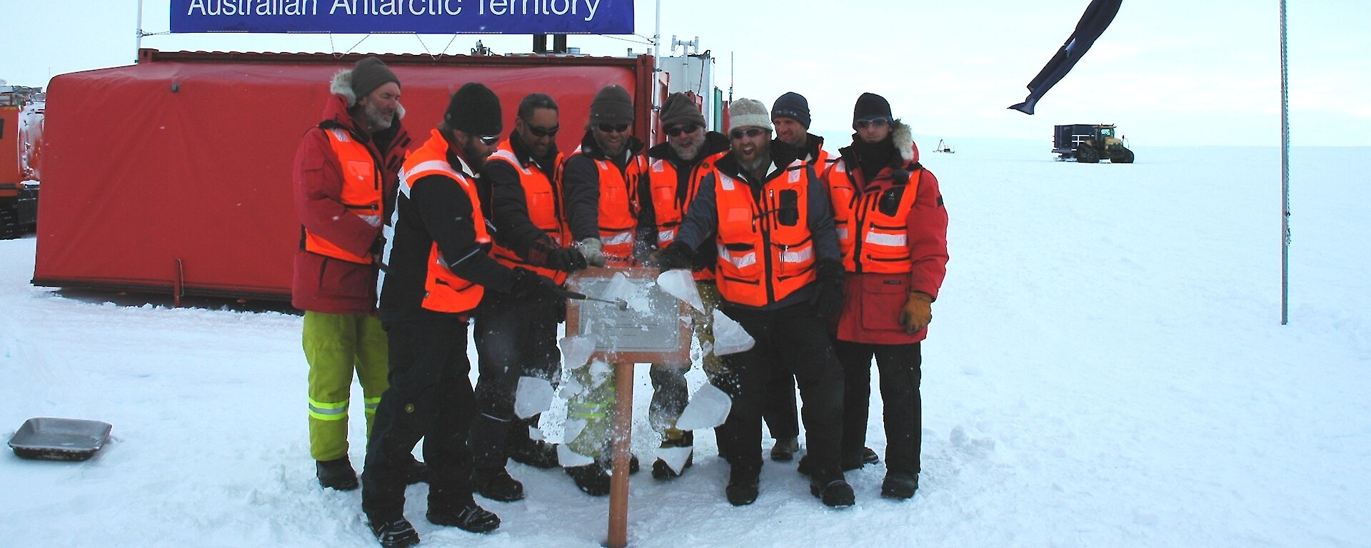 Eight expeditioners unveiling a plaque at Wilkins Runway as they cracked the ice encasing it.