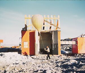 Weather observer preparing to release weather balloon in front of large balloon shed at Wilkes in 1961