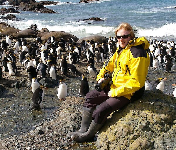 Expeditioner seated on rock with penguins in background