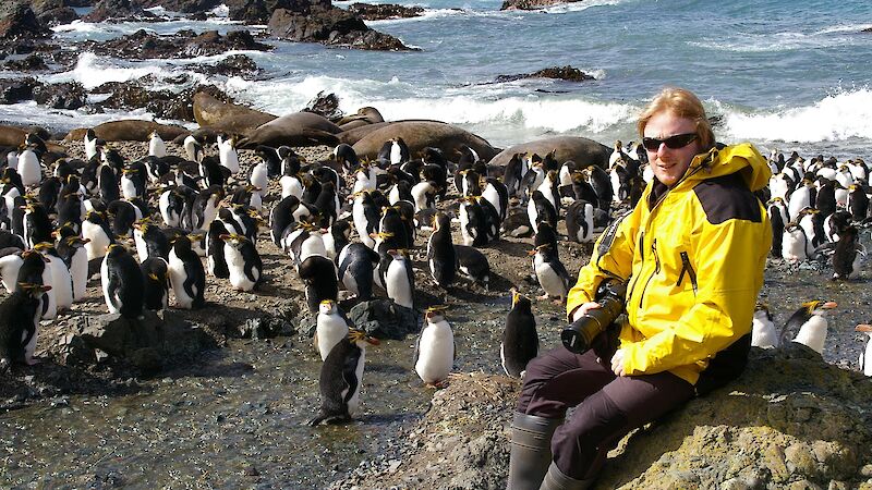Expeditioner seated on rock with penguins in background
