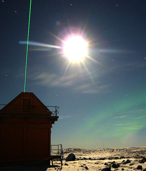The Davis lidar laser shoots upwards in the night sky, illuminated by a bright moon.