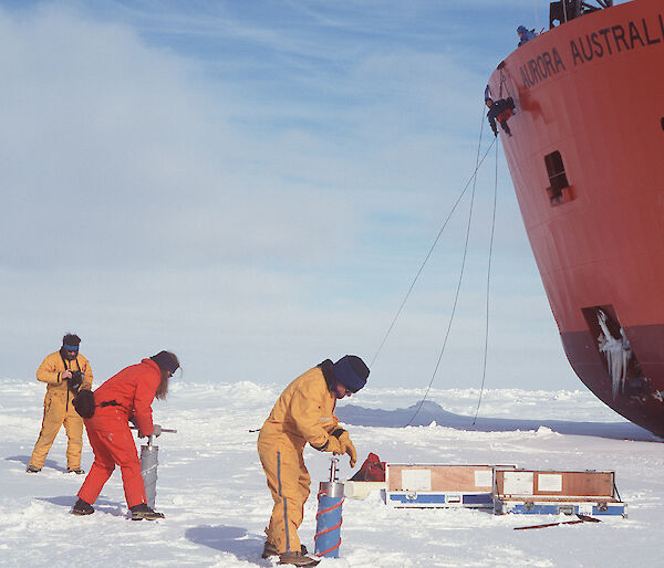 Expeditioners undertaking ice coring, with icebreaker ship in background