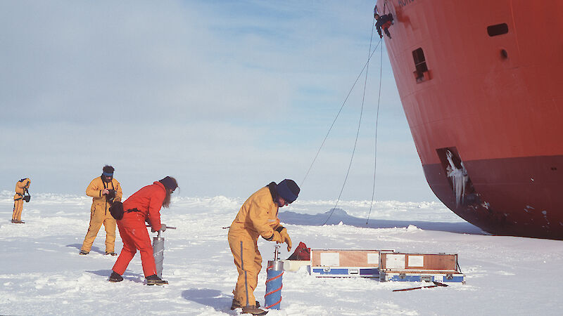 Expeditioners undertaking ice coring, with icebreaker ship in background
