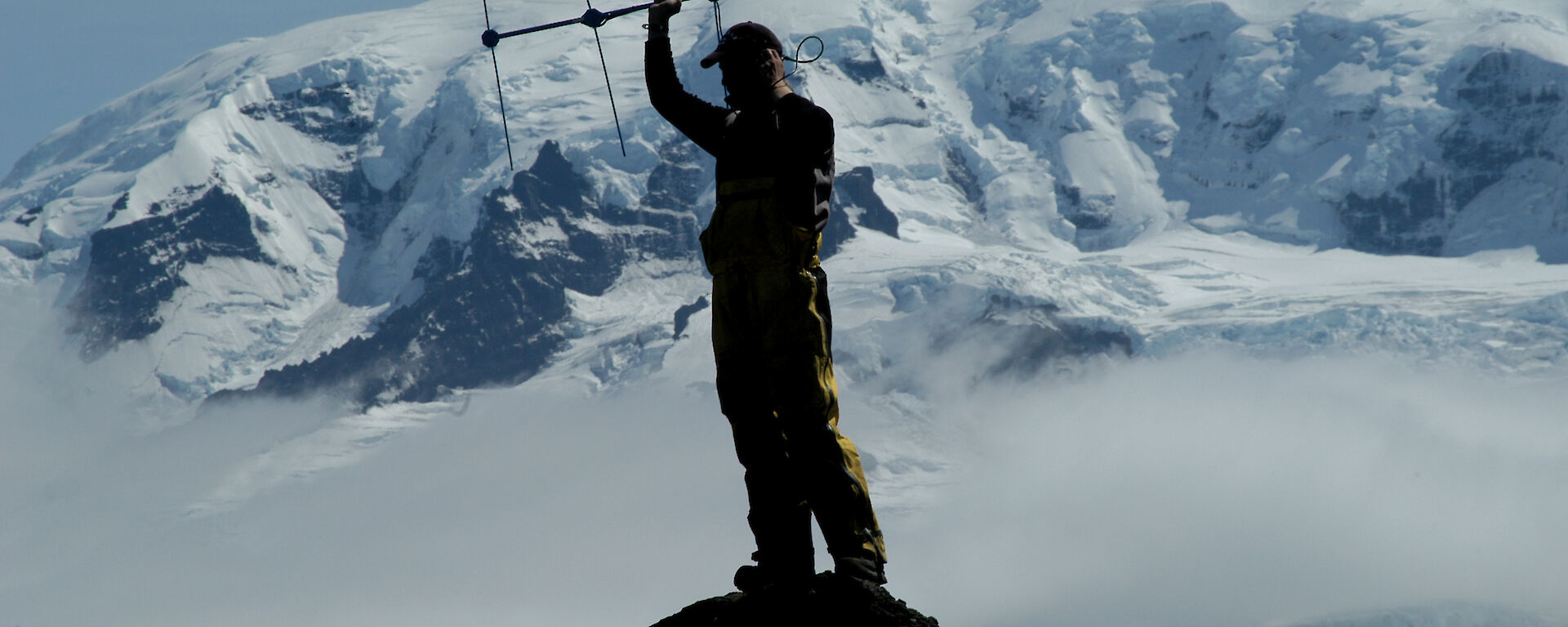 Expeditioner undertaking satellite tracking with ice cliff in background