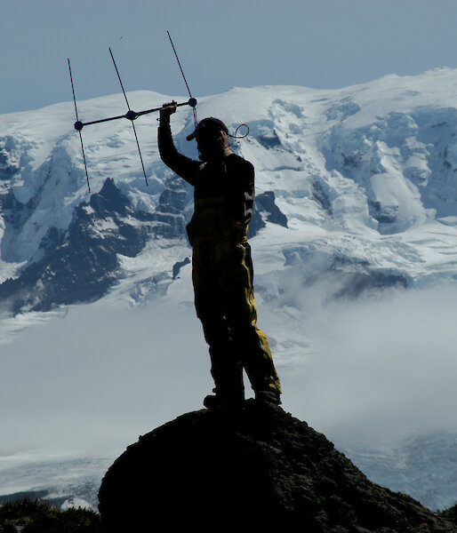 Expeditioner undertaking satellite tracking with ice cliff in background
