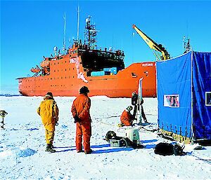 Expeditioners working on the sea ice with the Aurora Australis in the background