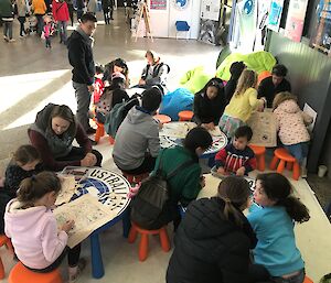 Children sitting at small tables colouring in calico bags.