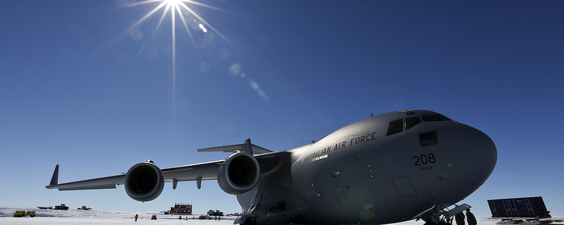 A grey cargo plane on a blue ice runway with the sun behind it.