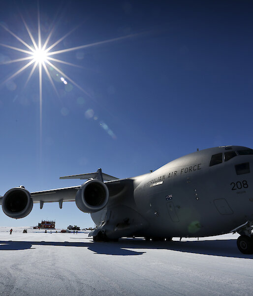 A grey cargo plane on a blue ice runway with the sun behind it.
