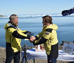 Two men wearing yellow jackets shaking hands.