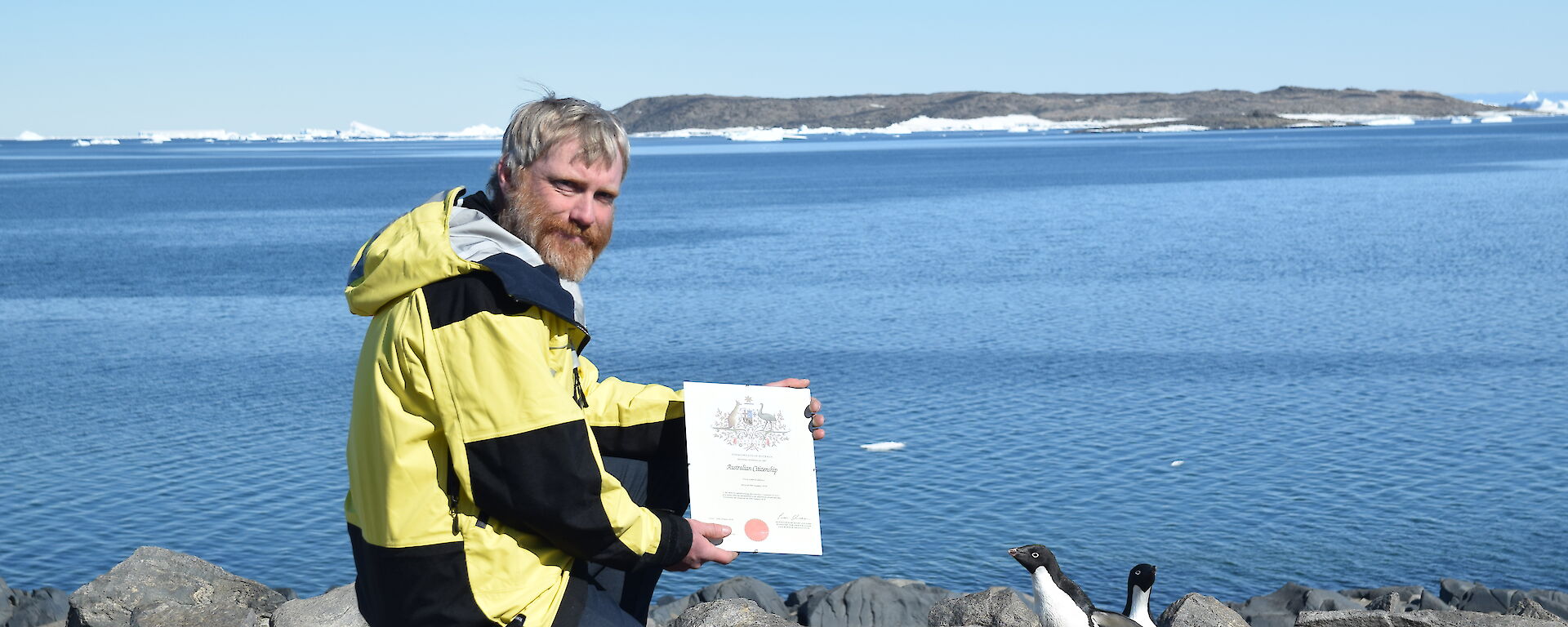 Man holding a certificate with two black and white penguins.