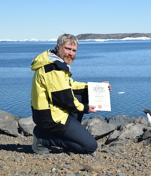 Man holding a certificate with two black and white penguins.