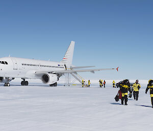Photo of expeditioners walking over ice runway with plane in the background.