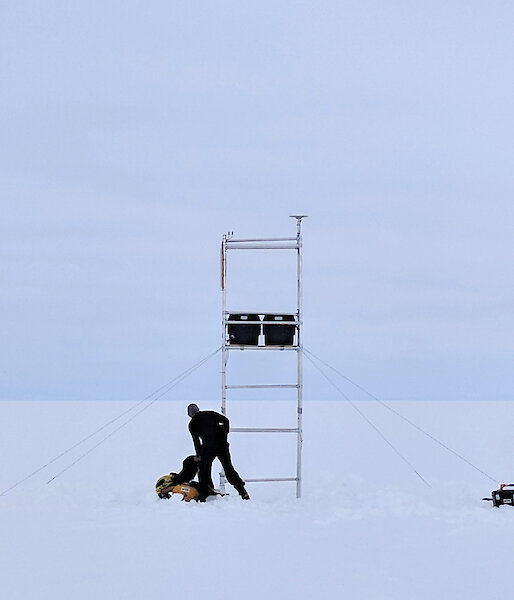 Two sillhouettes of people with instruments on scaffolding on a glacier