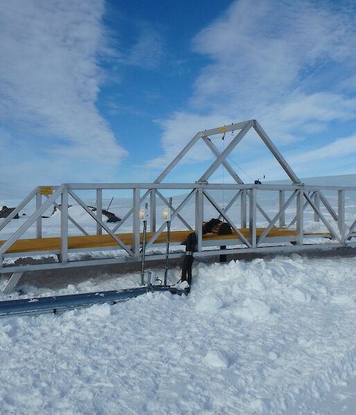 A bridge spanning the 8 metre-wide melt cavern on the Mawson plateau, to allow safe access to the melt bell. Pipework delivering hot water to the melt bell and returning fresh meltwater to the station can be seen in front.