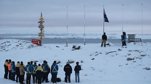 Casey research station expeditioners gather in front of the flag poles for Anzac Day service