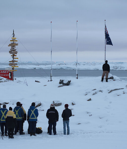 Casey research station expeditioners gather in front of the flag poles for Anzac Day service