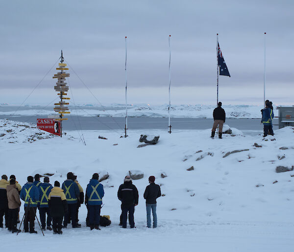 Casey research station expeditioners gather in front of the flag poles for Anzac Day service